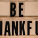 Black letters spell out "be thankful" on a sign.